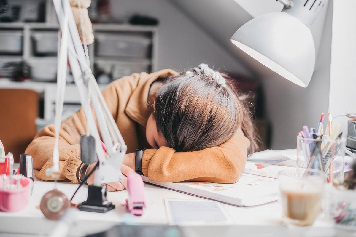 A pregnant teen laying her head on her desk.