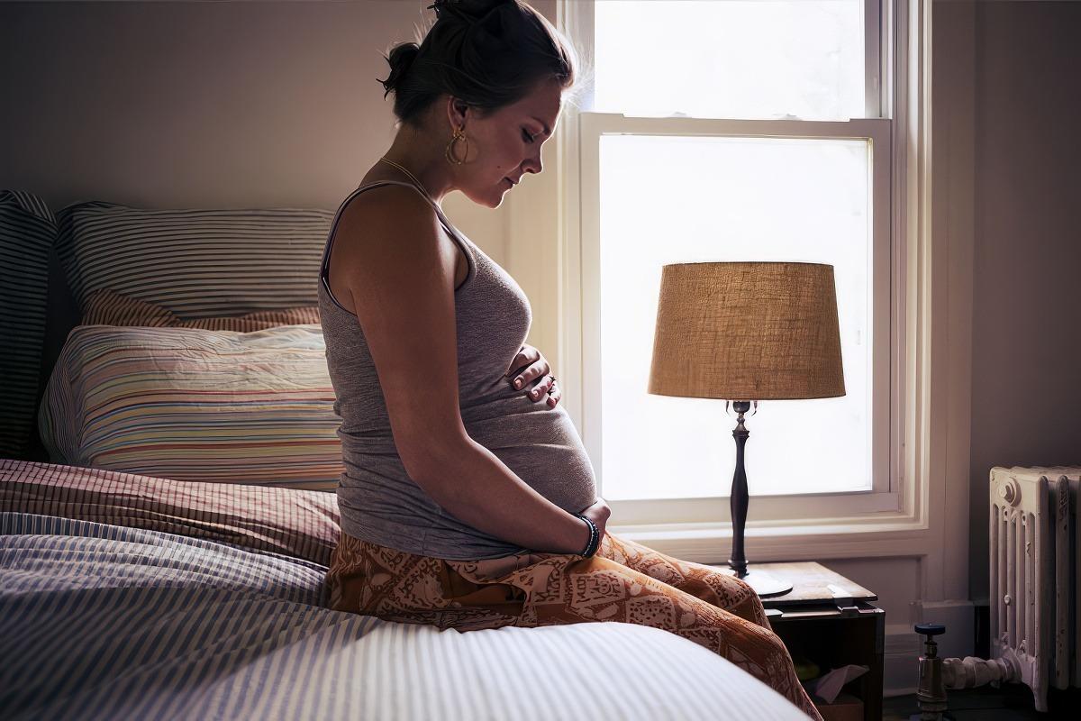 Delaware Perinatal Quality Collaborative: Pregnant mom sitting on bed holding her belly