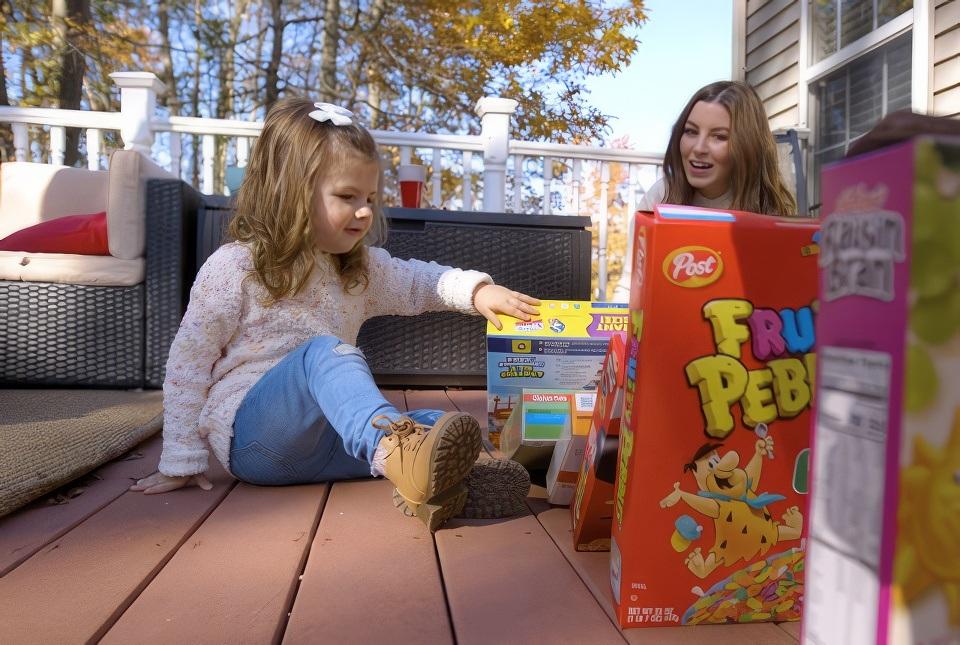 A child age 0-3 and her mom playing outside with cereal boxes.